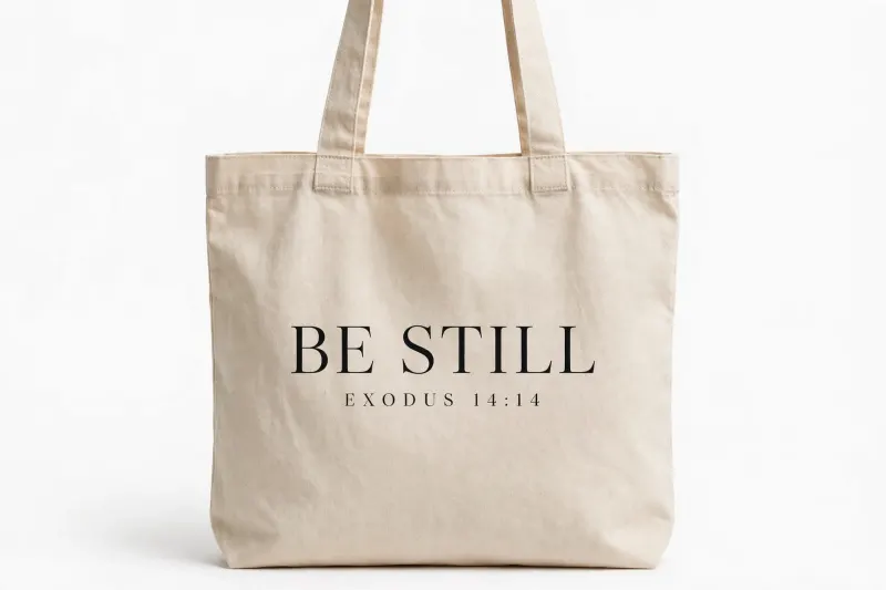 Natural canvas tote printed “BE STILL — EXODUS 14:14”